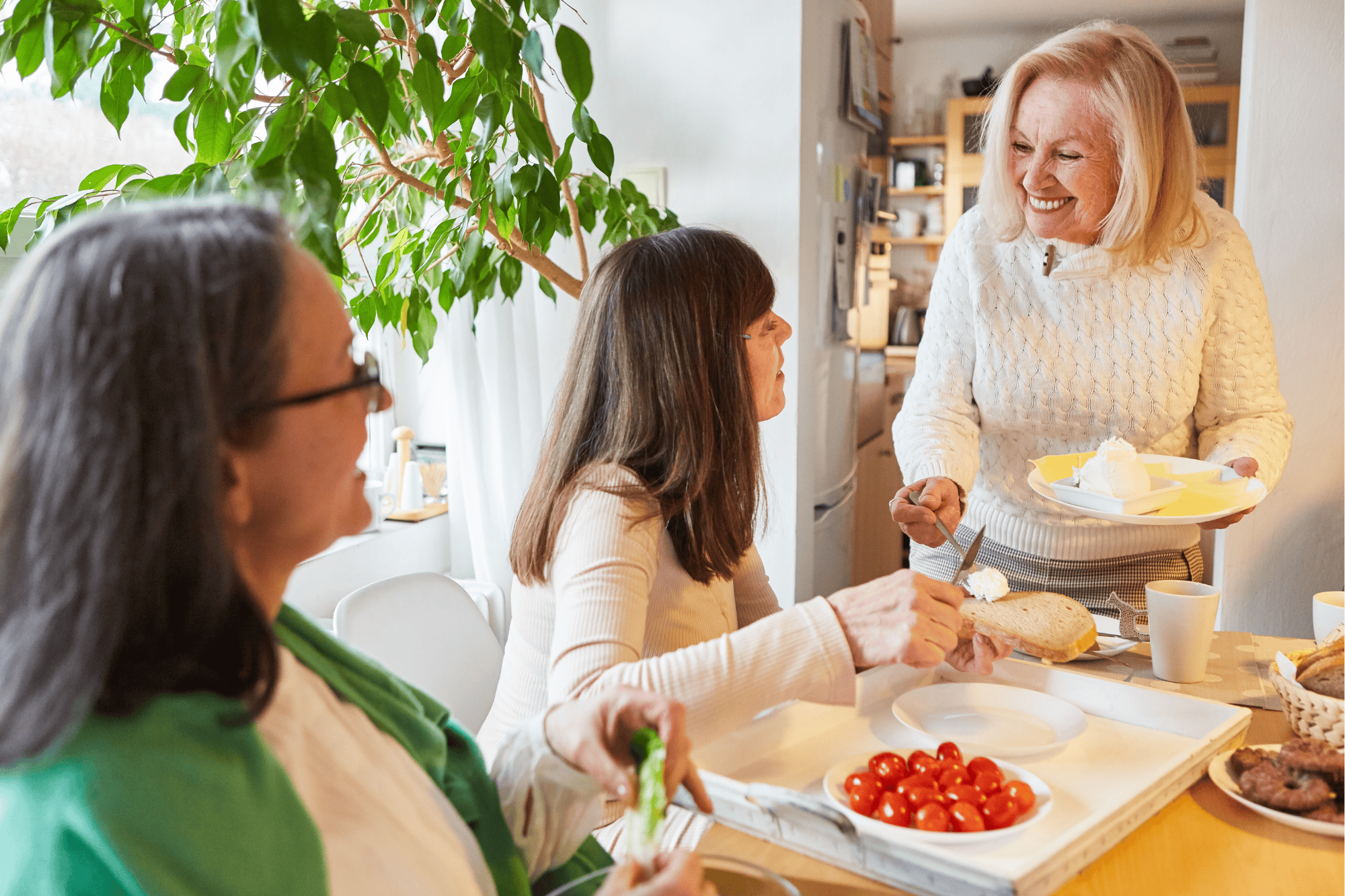 Three women sharing food and conversation in a bright kitchen, enjoying a meal together
